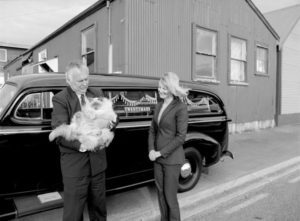Adrian & Julie Catran, directors of Twentymans, cradle Tommie the funeral home’s corpulent feline, beside the company’s 1939 Chevrolet hearse, parked outside the joinery workshop where Robert Twentyman manufactured caskets from circa 1924. Photograph by Peter Quinn